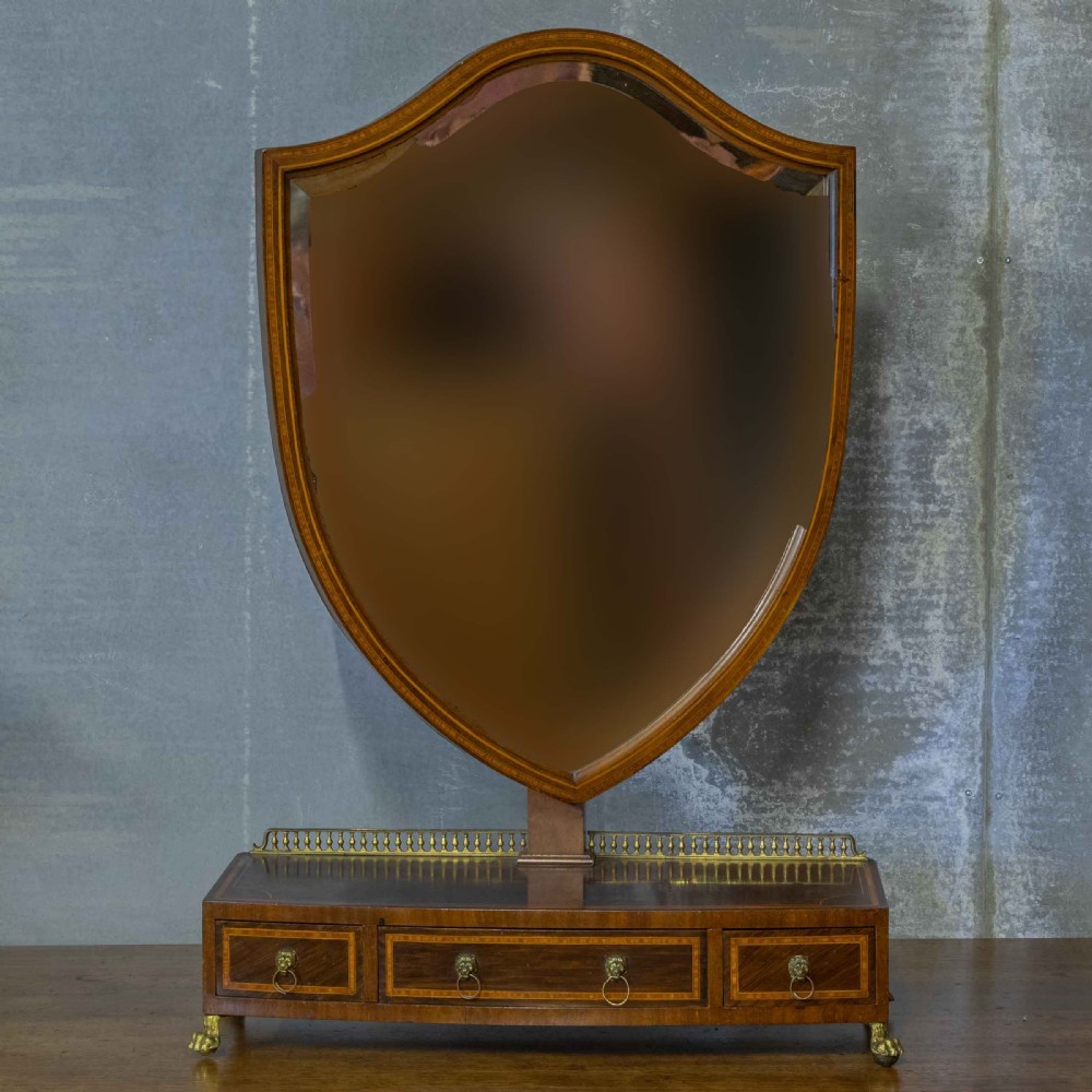 An Edwardian mahogany shield-shaped swing toilet mirror resting on a boxwood inlaid base with drawers and brass feet.