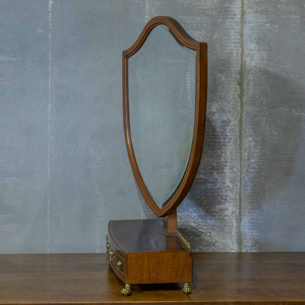 An Edwardian mahogany shield-shaped swing toilet mirror resting on a boxwood inlaid base with drawers and brass feet. View IV