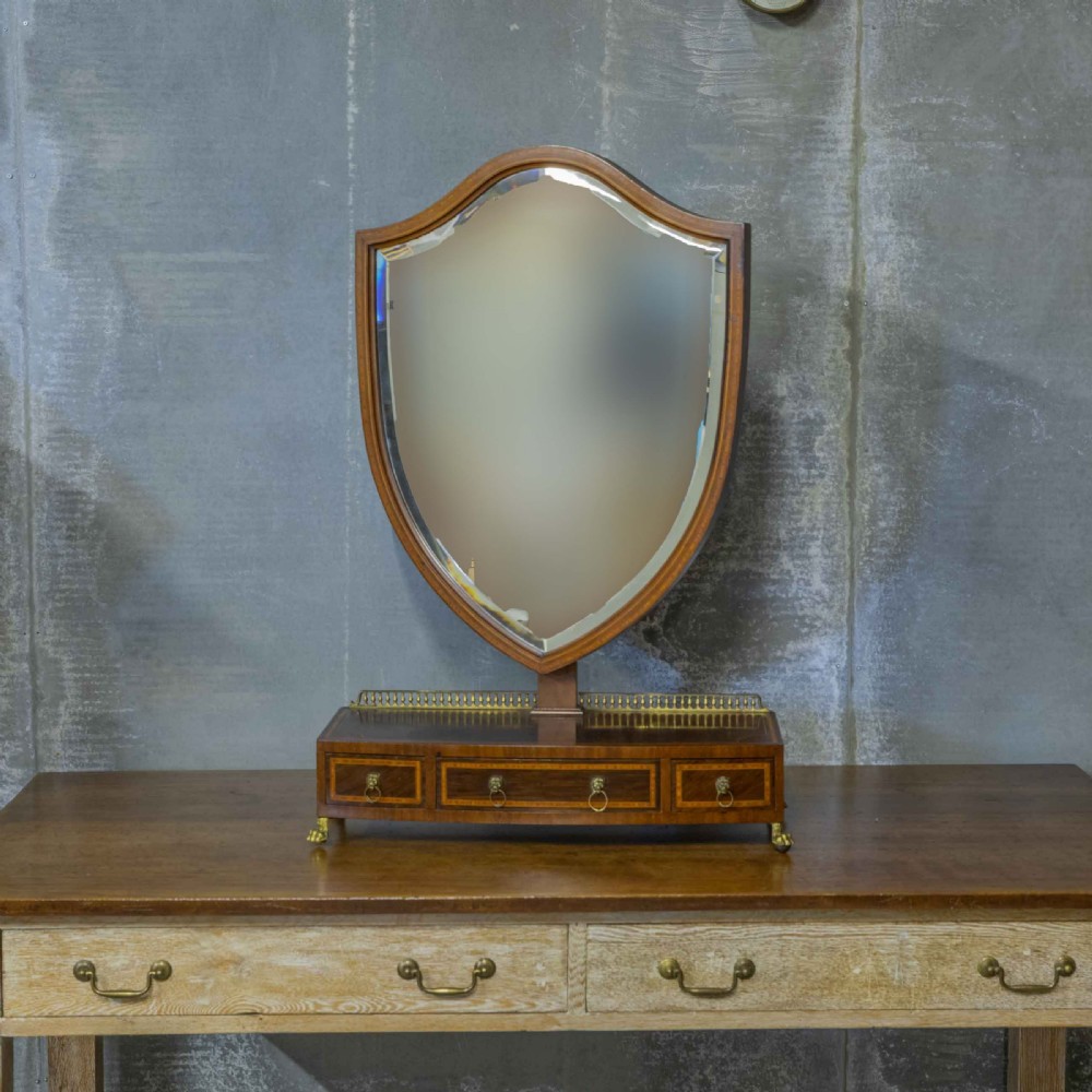 An Edwardian mahogany shield-shaped swing toilet mirror resting on a boxwood inlaid base with drawers and brass feet. View V