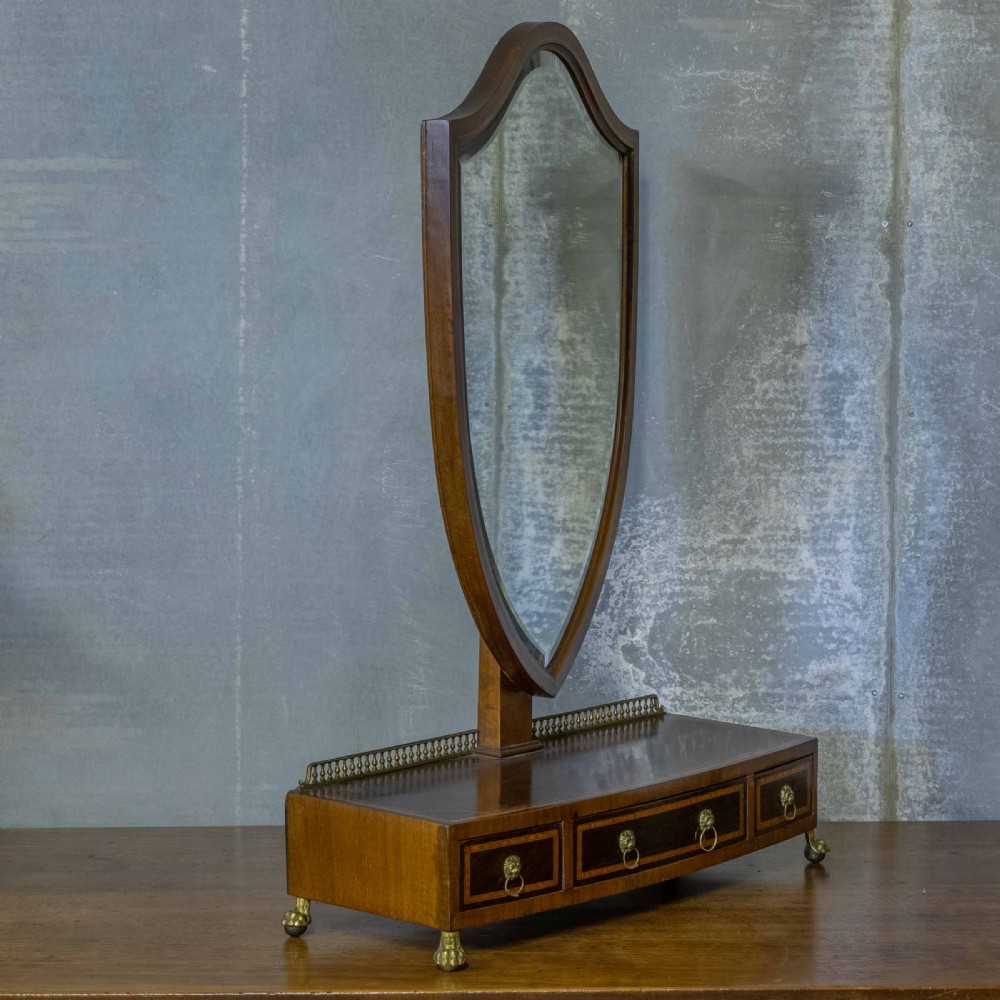 An Edwardian mahogany shield-shaped swing toilet mirror resting on a boxwood inlaid base with drawers and brass feet. View VI