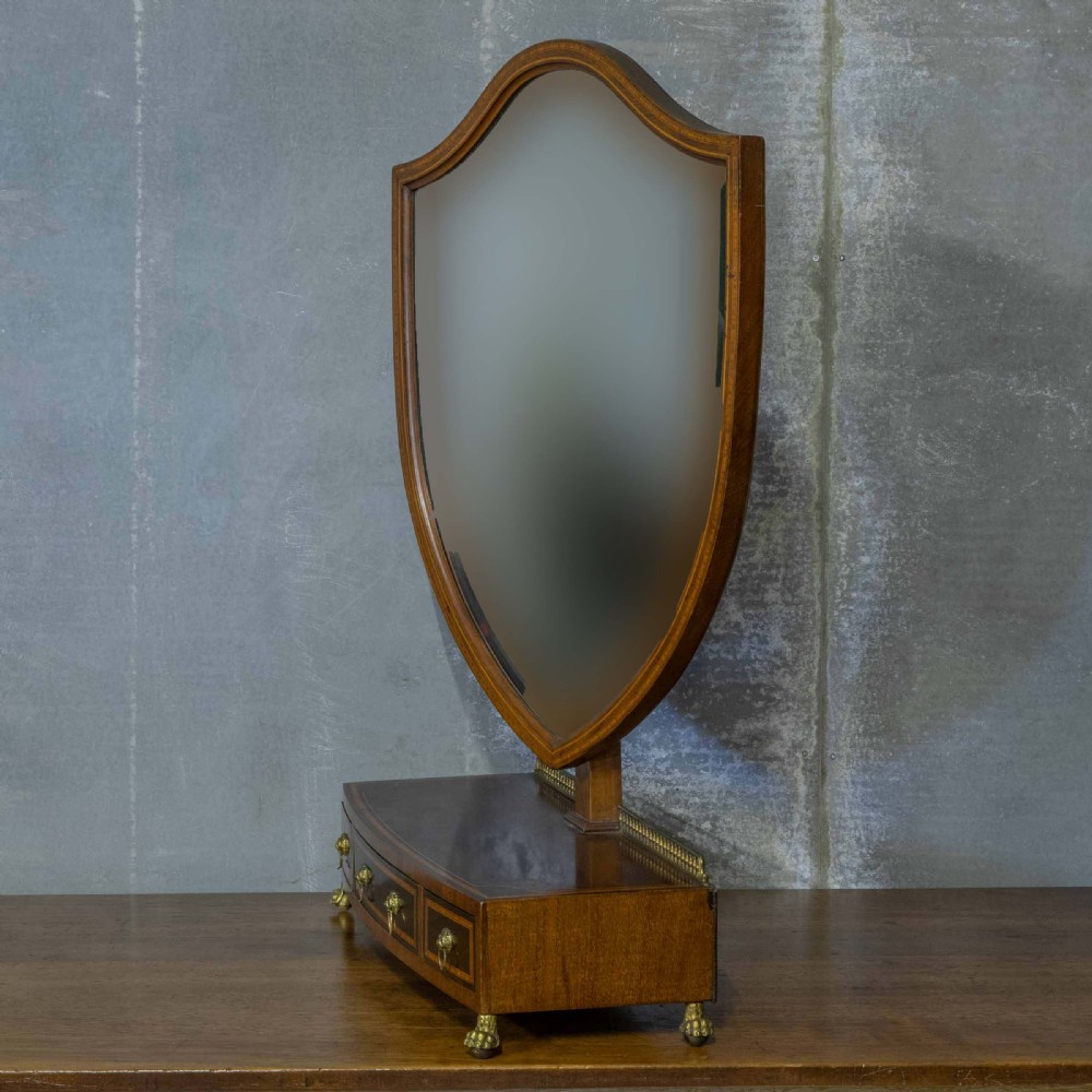 An Edwardian mahogany shield-shaped swing toilet mirror resting on a boxwood inlaid base with drawers and brass feet. View IX