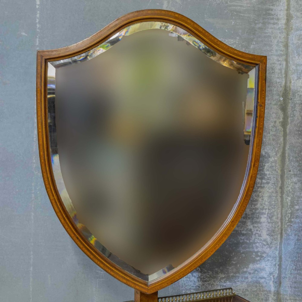 An Edwardian mahogany shield-shaped swing toilet mirror resting on a boxwood inlaid base with drawers and brass feet. View XVI