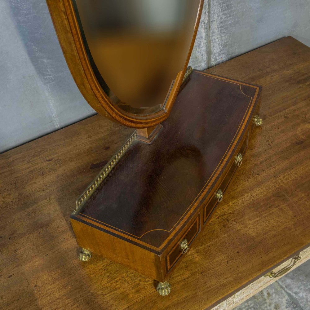 An Edwardian mahogany shield-shaped swing toilet mirror resting on a boxwood inlaid base with drawers and brass feet. View XVII