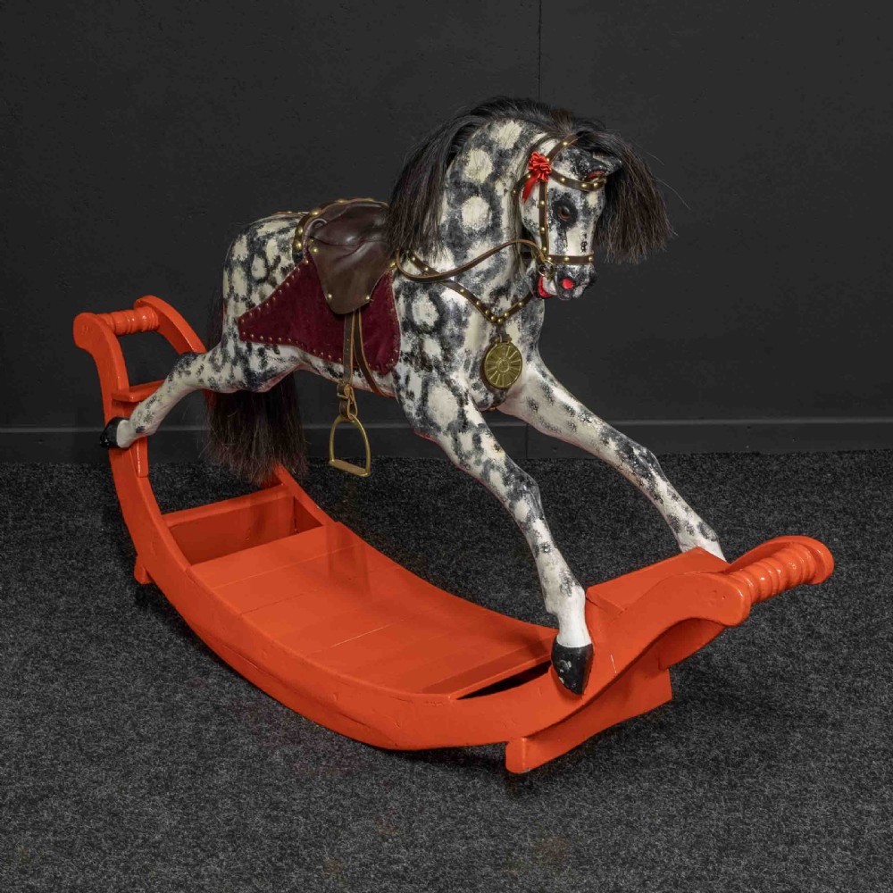 An antique Victorian hand-painted dappled grey wooden rocking horse with a leather saddle and horsehair mane mounted on an orange bow rocker.