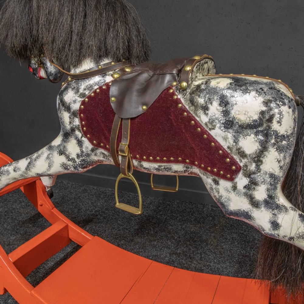 An antique Victorian hand-painted dappled grey wooden rocking horse with a leather saddle and horsehair mane mounted on an orange bow rocker. View II