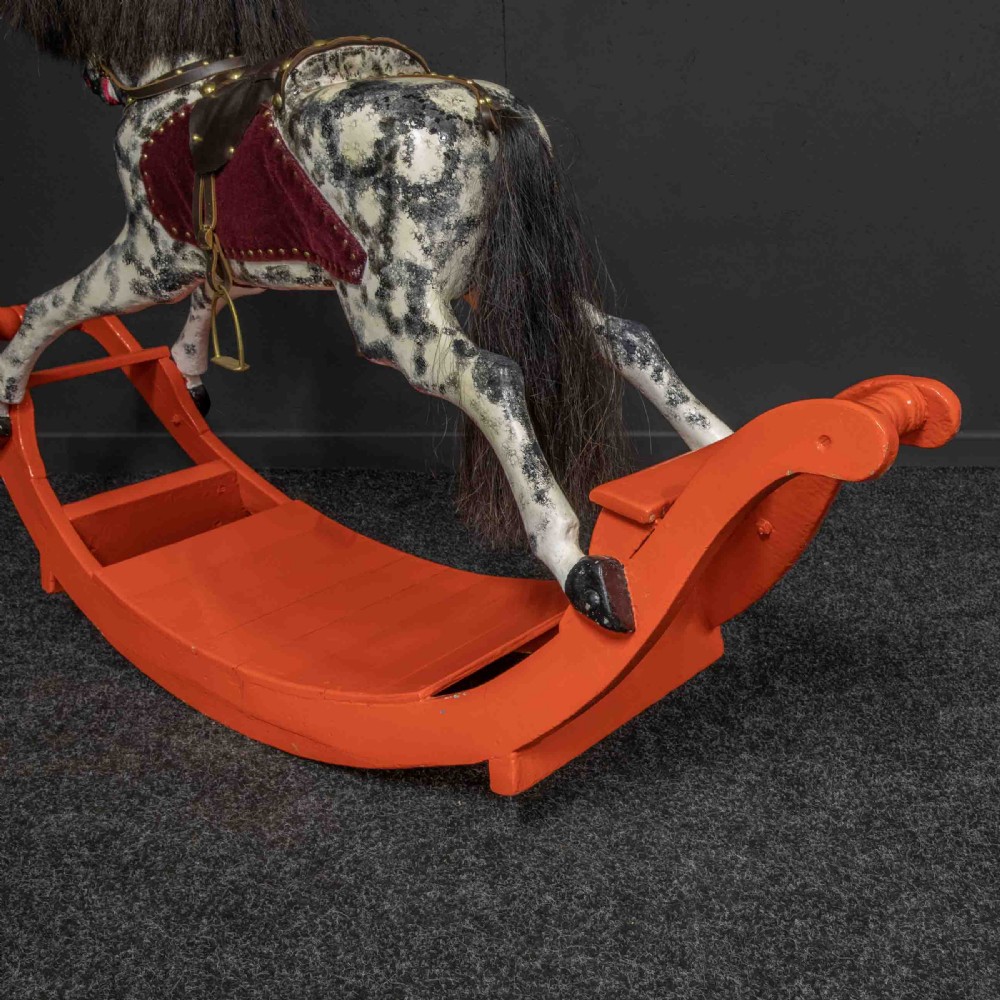 An antique Victorian hand-painted dappled grey wooden rocking horse with a leather saddle and horsehair mane mounted on an orange bow rocker. View VII