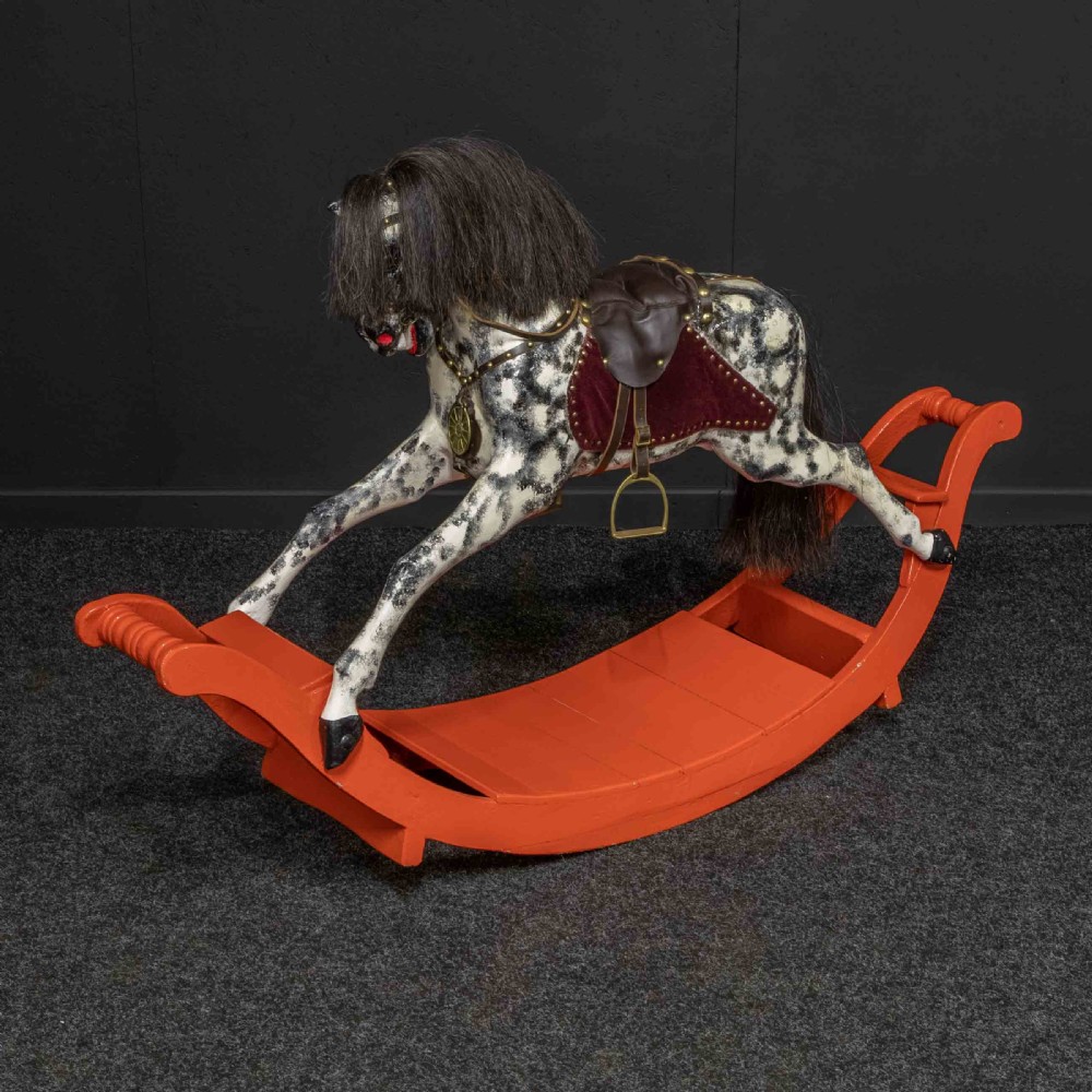 An antique Victorian hand-painted dappled grey wooden rocking horse with a leather saddle and horsehair mane mounted on an orange bow rocker. View X