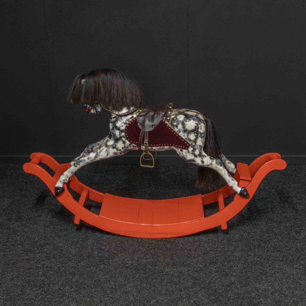 An antique Victorian hand-painted dappled grey wooden rocking horse with a leather saddle and horsehair mane mounted on an orange bow rocker. View XI