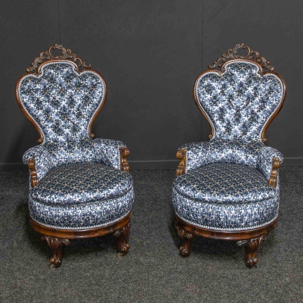A pair of Victorian armchairs with carved timber frames, blue patterned button-back fabric upholstery, and rounded seat cushions on brass castors.
