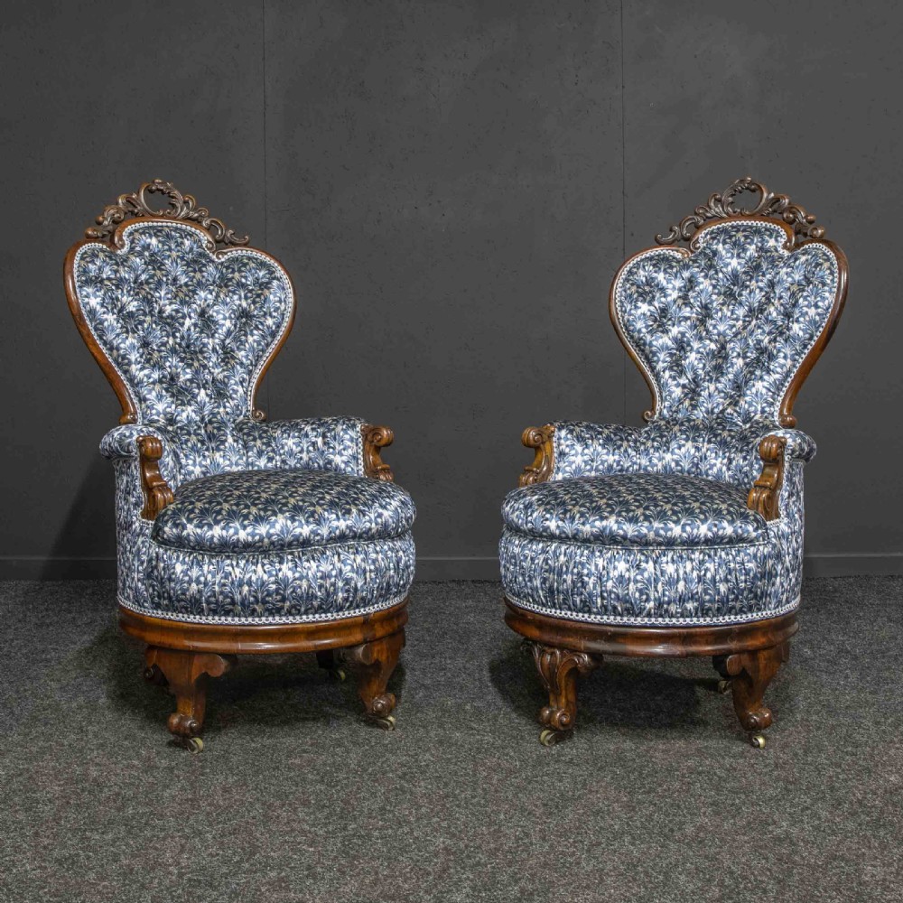 A pair of Victorian armchairs with carved timber frames, blue patterned button-back fabric upholstery, and rounded seat cushions on brass castors. View II