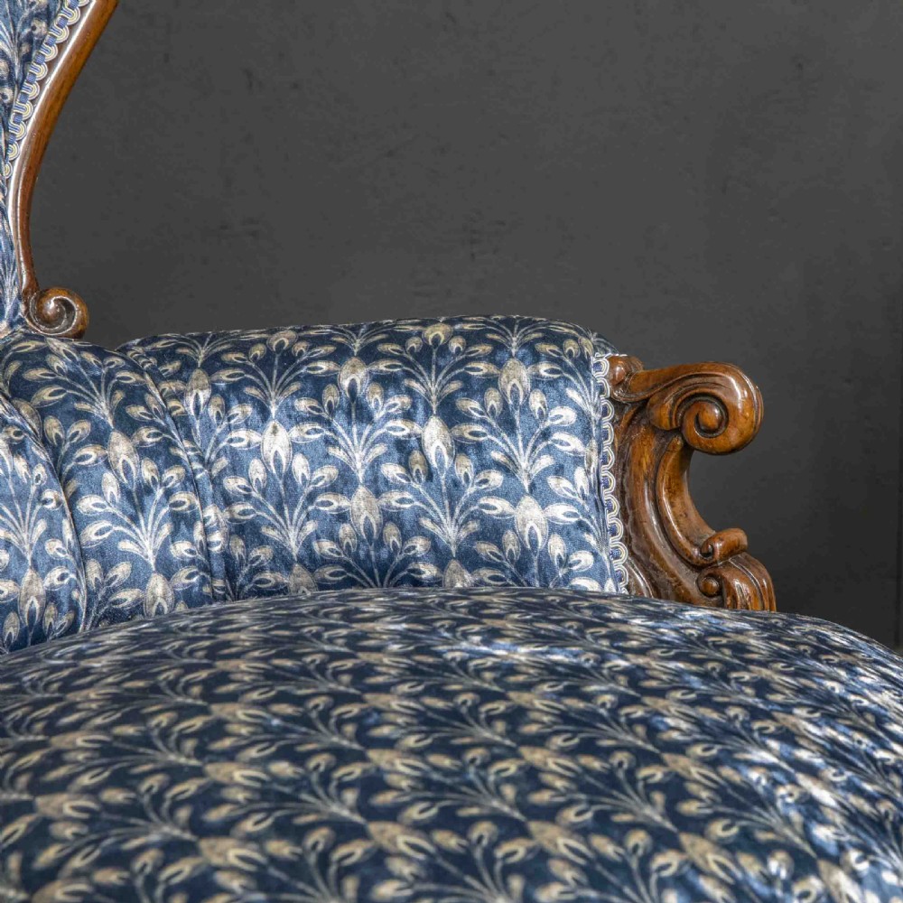 A pair of Victorian armchairs with carved timber frames, blue patterned button-back fabric upholstery, and rounded seat cushions on brass castors. View III