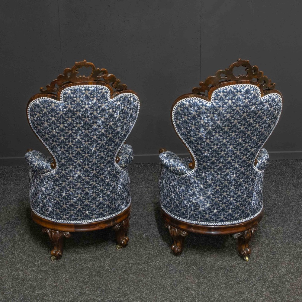 A pair of Victorian armchairs with carved timber frames, blue patterned button-back fabric upholstery, and rounded seat cushions on brass castors. View VI
