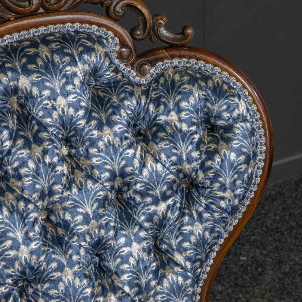 A pair of Victorian armchairs with carved timber frames, blue patterned button-back fabric upholstery, and rounded seat cushions on brass castors. View X