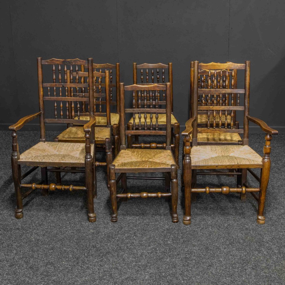 A set of eight dark oak Lancashire spindleback dining chairs with hand-woven rush seats, comprising six side chairs and two carver armchairs.
