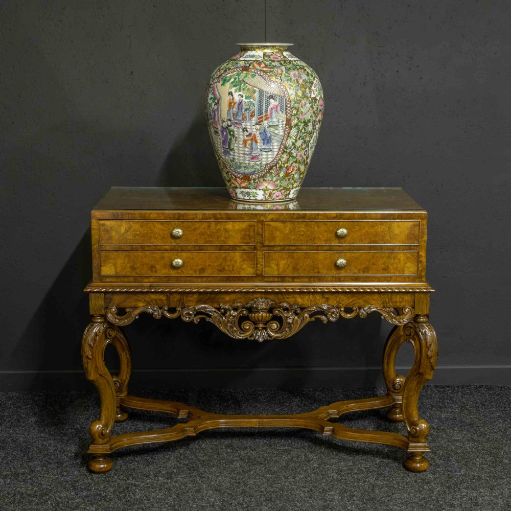A burr walnut chest on stand featuring four drawers with brass knobs, an intricately carved foliate apron, cabriole legs, and a shaped stretcher base. View II