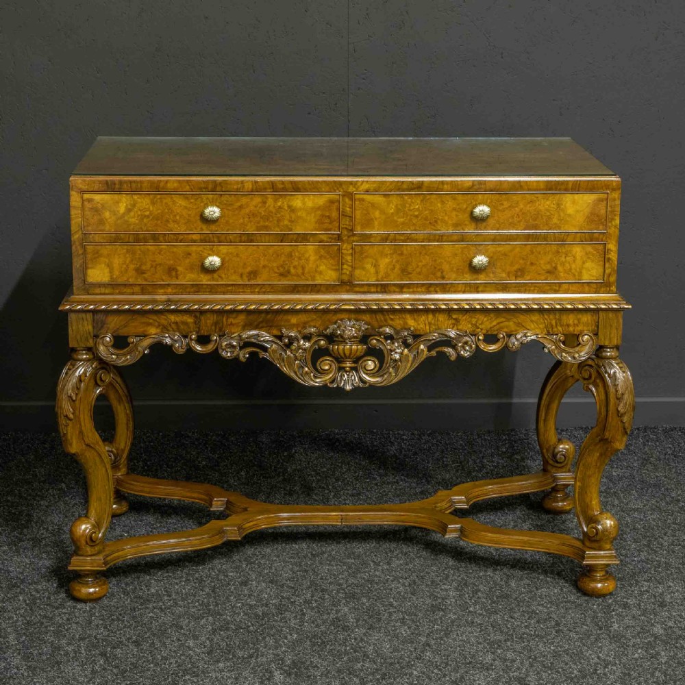 A burr walnut chest on stand featuring four drawers with brass knobs, an intricately carved foliate apron, cabriole legs, and a shaped stretcher base. View III