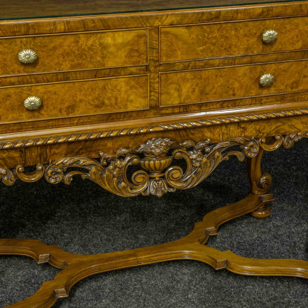 A burr walnut chest on stand featuring four drawers with brass knobs, an intricately carved foliate apron, cabriole legs, and a shaped stretcher base. View V