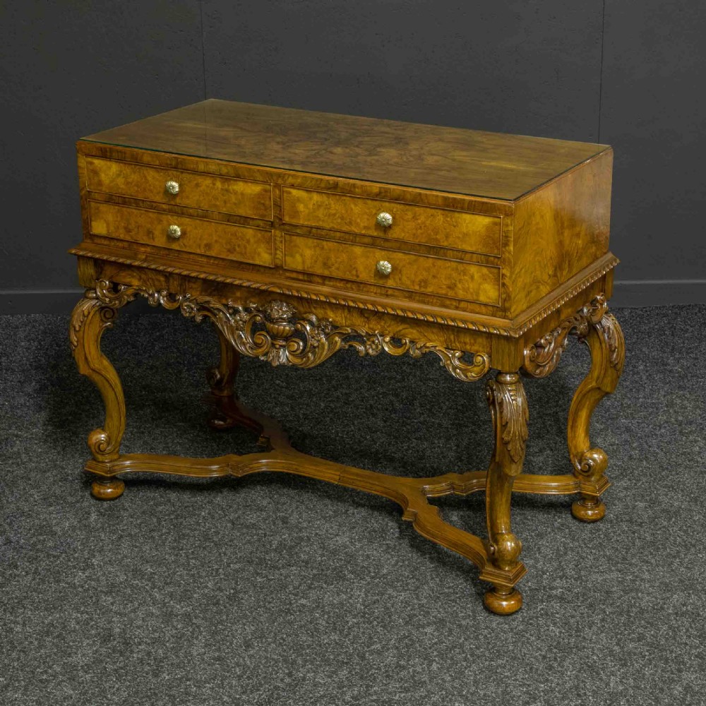 A burr walnut chest on stand featuring four drawers with brass knobs, an intricately carved foliate apron, cabriole legs, and a shaped stretcher base. View IX
