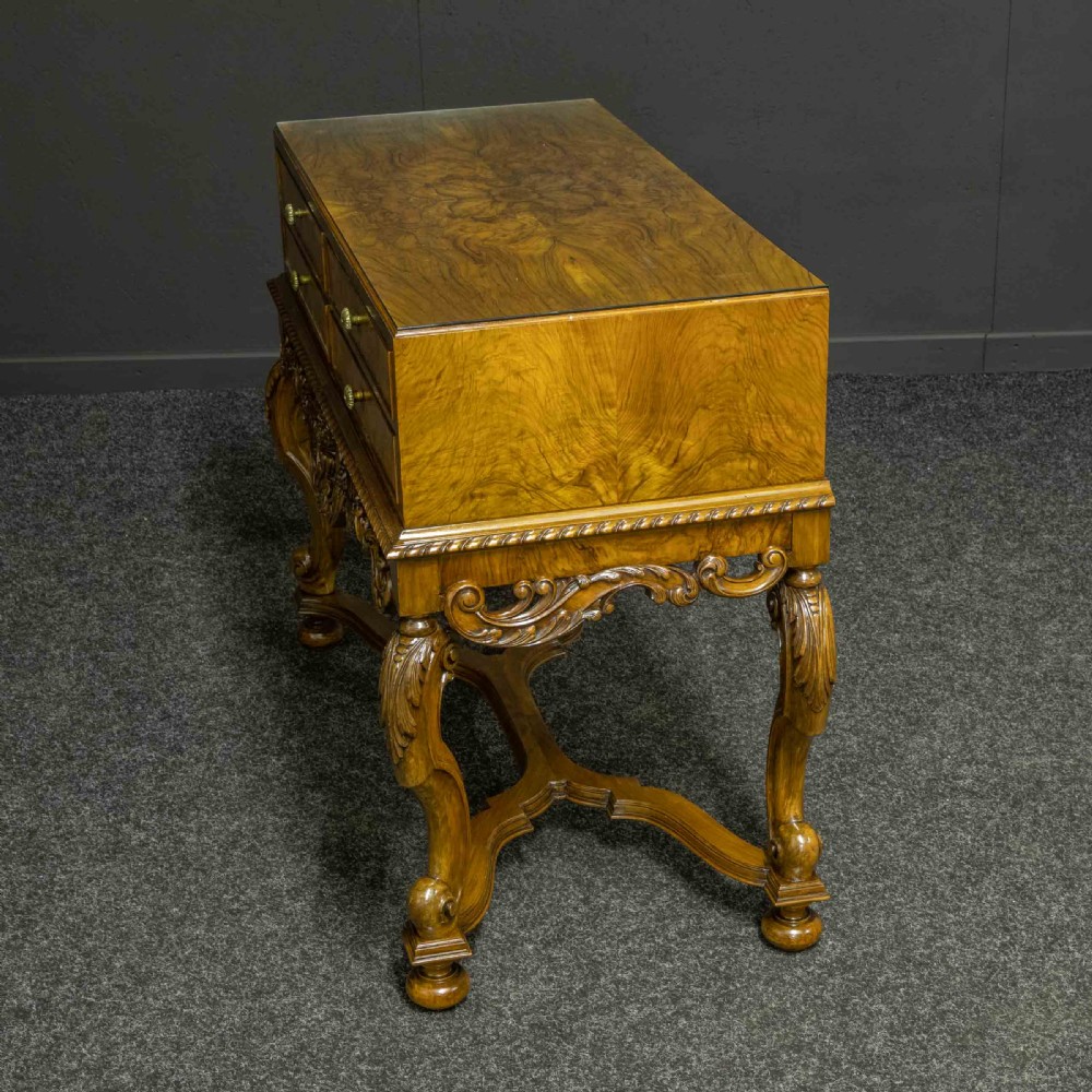 A burr walnut chest on stand featuring four drawers with brass knobs, an intricately carved foliate apron, cabriole legs, and a shaped stretcher base. View X