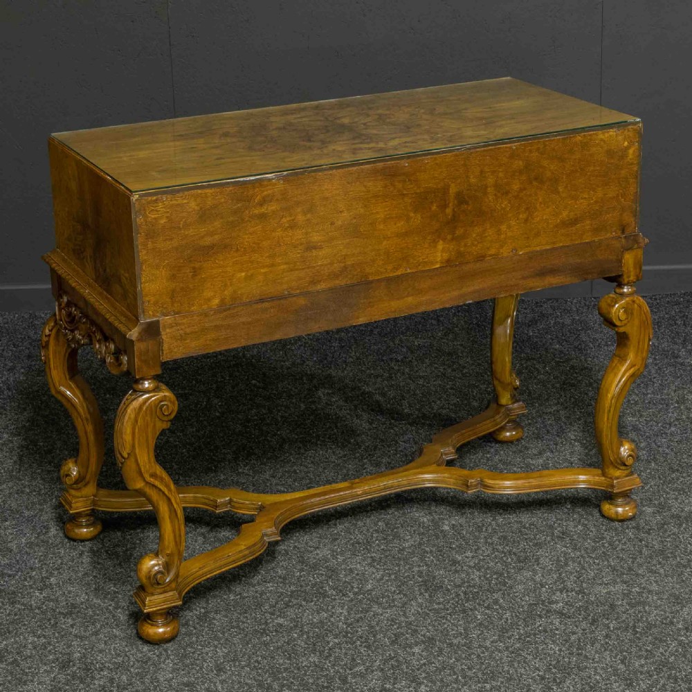 A burr walnut chest on stand featuring four drawers with brass knobs, an intricately carved foliate apron, cabriole legs, and a shaped stretcher base. View XI