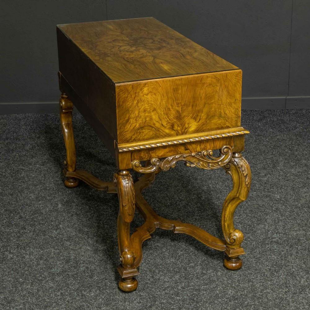 A burr walnut chest on stand featuring four drawers with brass knobs, an intricately carved foliate apron, cabriole legs, and a shaped stretcher base. View XII