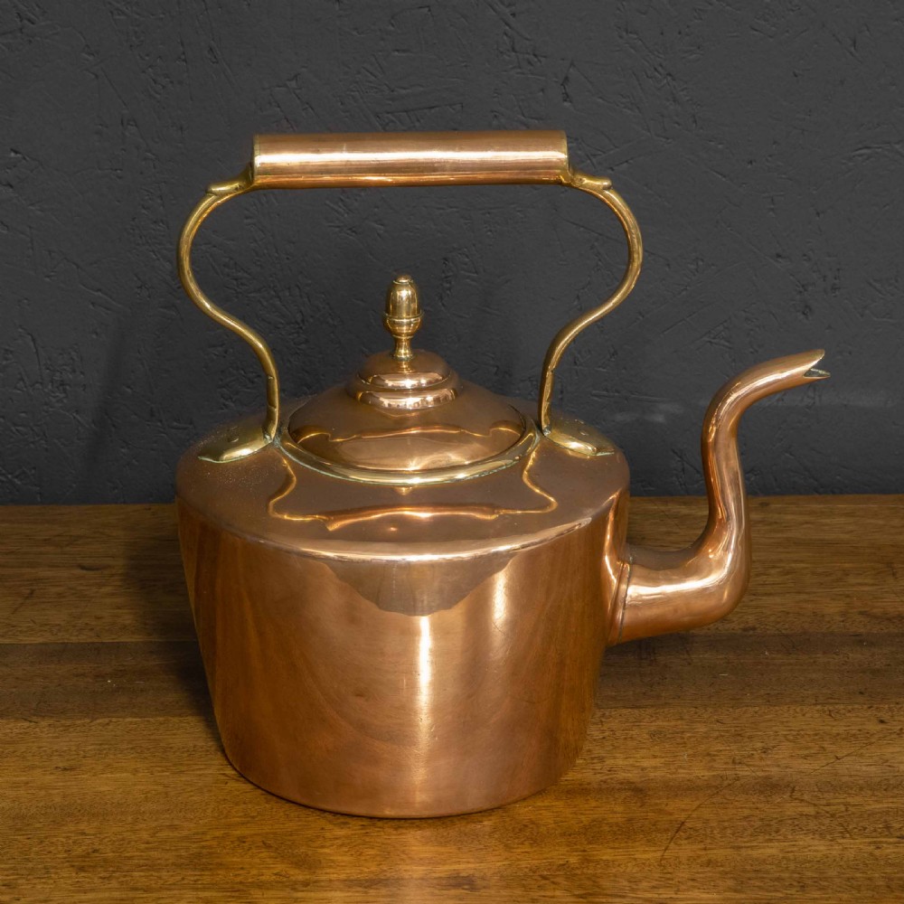 A polished Victorian copper kettle featuring a brass finial lid, a curved spout, and an overhead copper handle with brass supports.