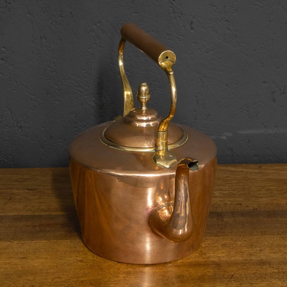 A polished Victorian copper kettle featuring a brass finial lid, a curved spout, and an overhead copper handle with brass supports. View III