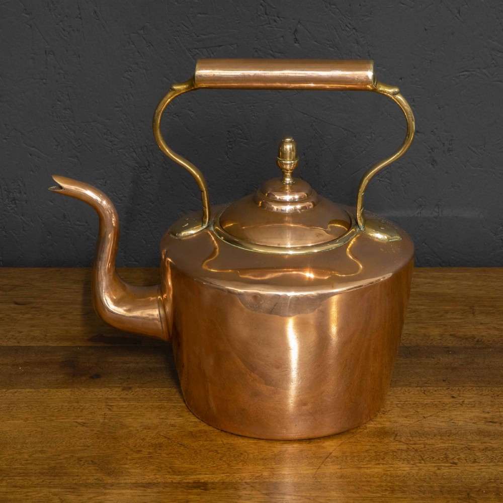 A polished Victorian copper kettle featuring a brass finial lid, a curved spout, and an overhead copper handle with brass supports. View IV