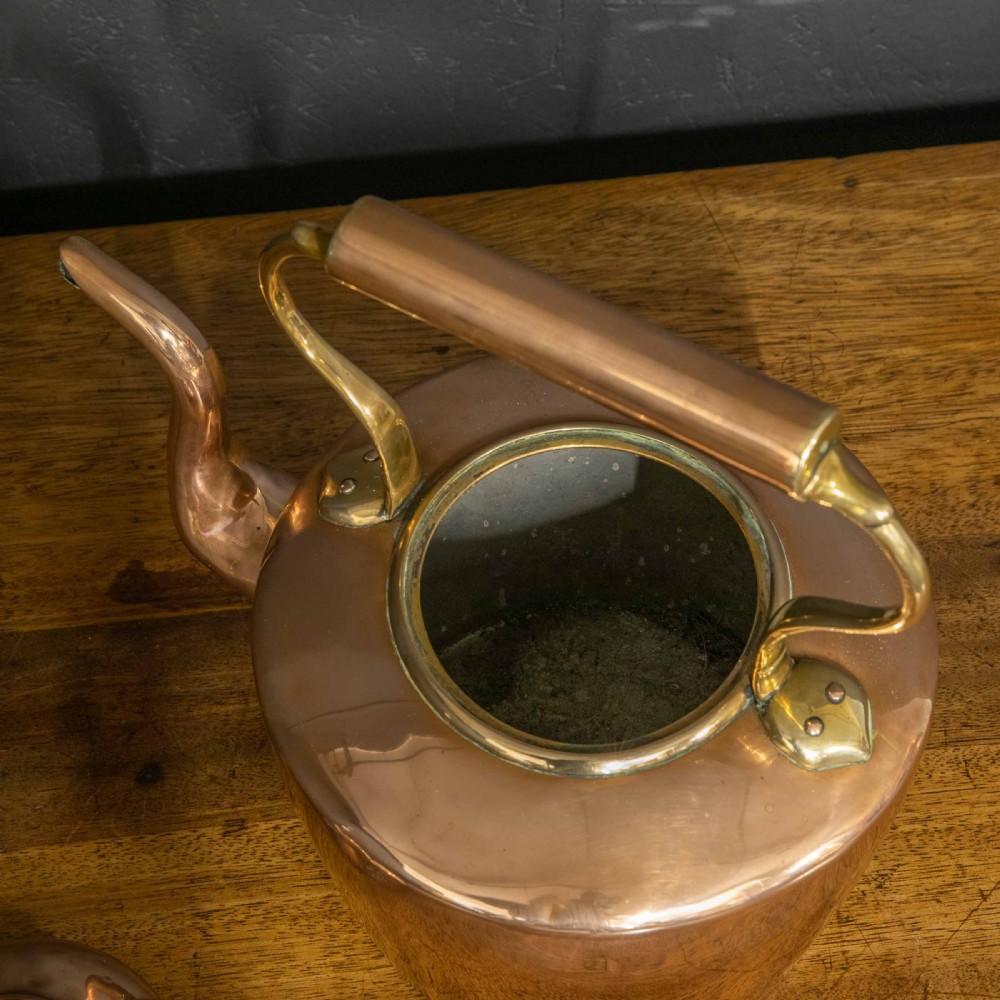 A polished Victorian copper kettle featuring a brass finial lid, a curved spout, and an overhead copper handle with brass supports. View VII