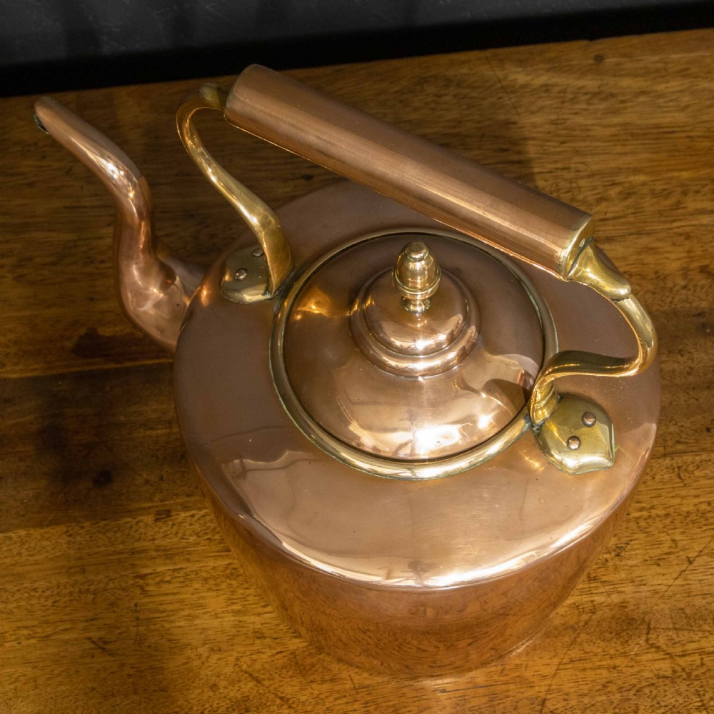 A polished Victorian copper kettle featuring a brass finial lid, a curved spout, and an overhead copper handle with brass supports. View VIII