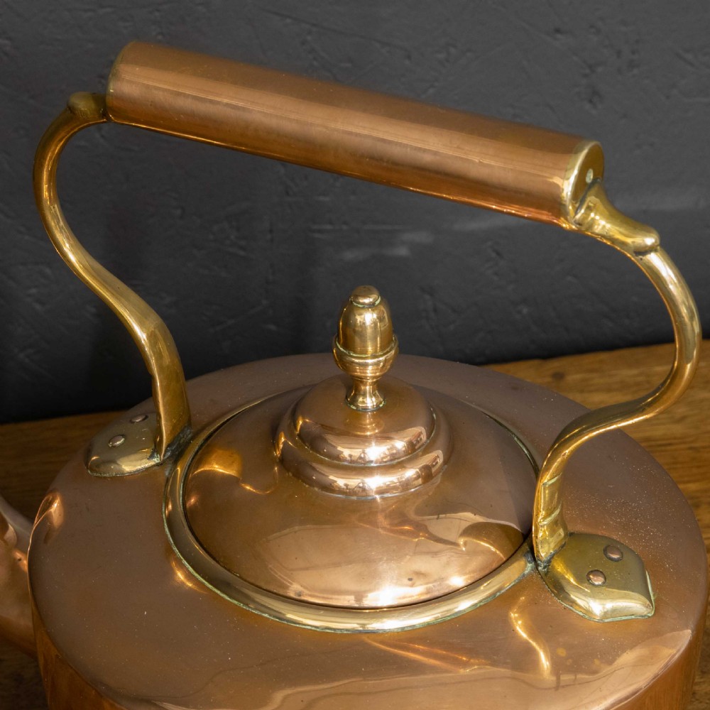 A polished Victorian copper kettle featuring a brass finial lid, a curved spout, and an overhead copper handle with brass supports. View IX