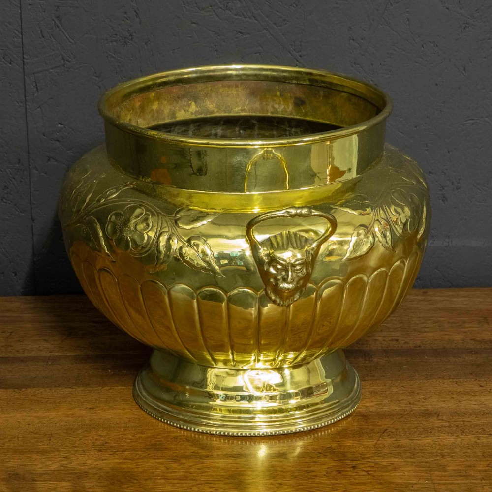 A polished brass planter featuring embossed floral motifs, gadrooned lower body detailing, twin side handles, and a raised pedestal base. View II