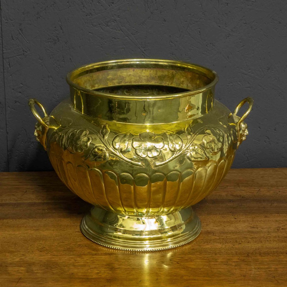 A polished brass planter featuring embossed floral motifs, gadrooned lower body detailing, twin side handles, and a raised pedestal base. View III