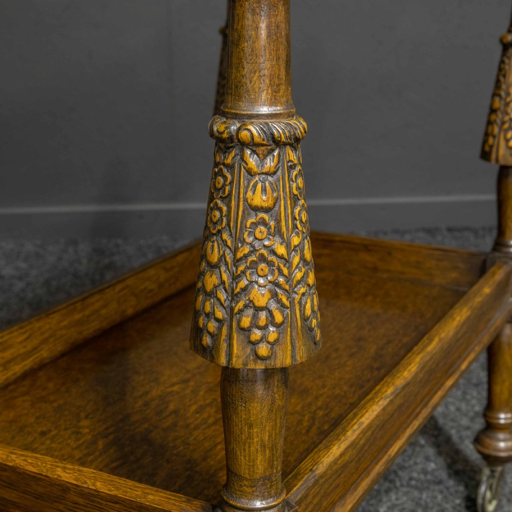 A dark oak two-tier tea trolley with carved turned legs, a galleried top tray, and metal castors. View II