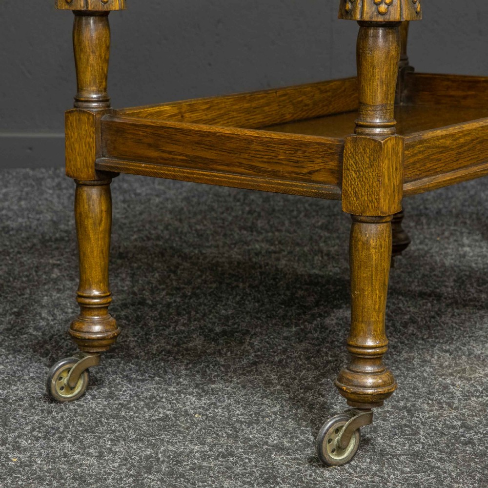 A dark oak two-tier tea trolley with carved turned legs, a galleried top tray, and metal castors. View VI