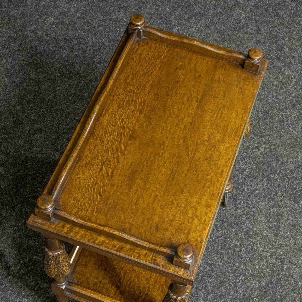 A dark oak two-tier tea trolley with carved turned legs, a galleried top tray, and metal castors. View IX