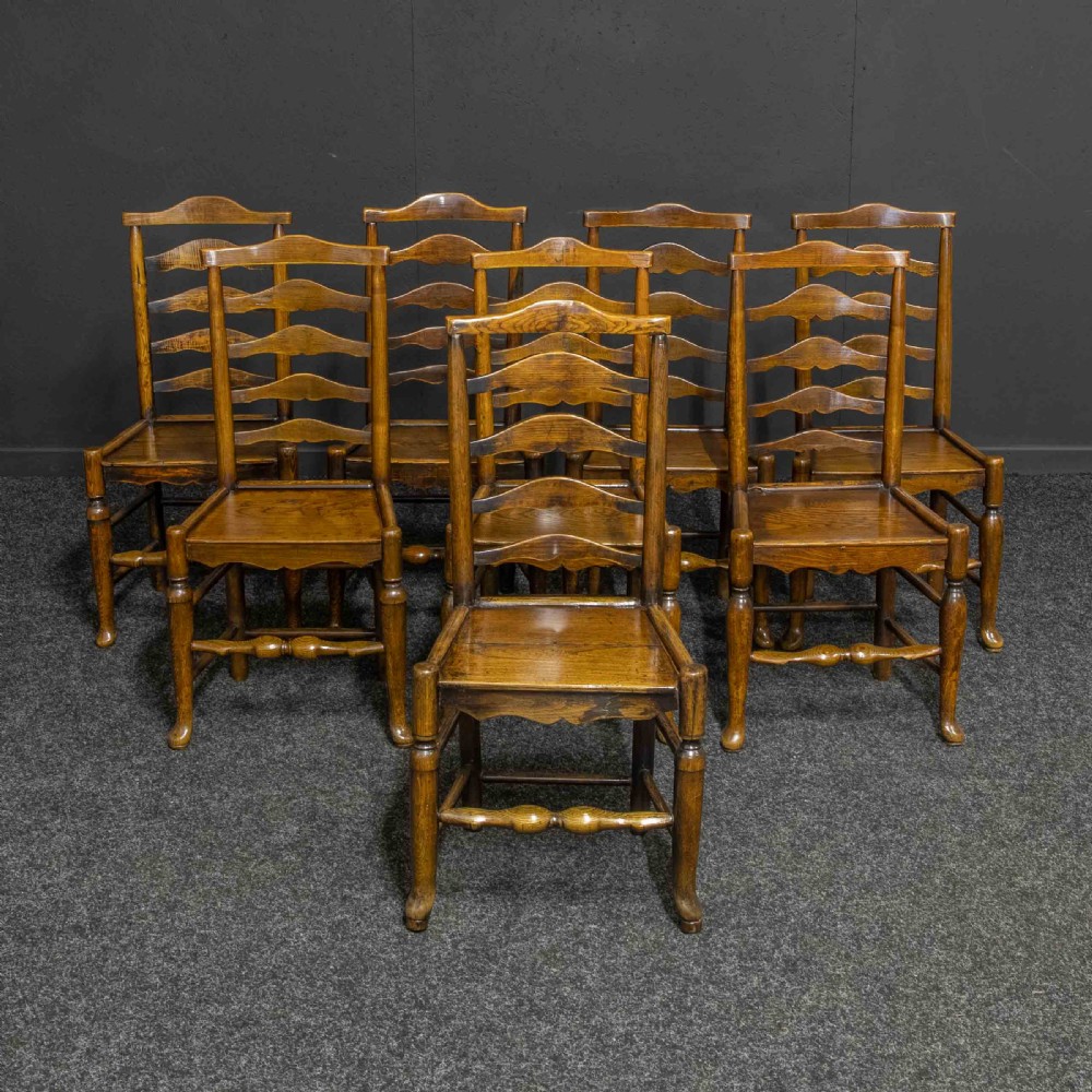 A set of eight Georgian oak dining chairs featuring wavy ladderback splats, solid wooden seats, and turned front stretchers.