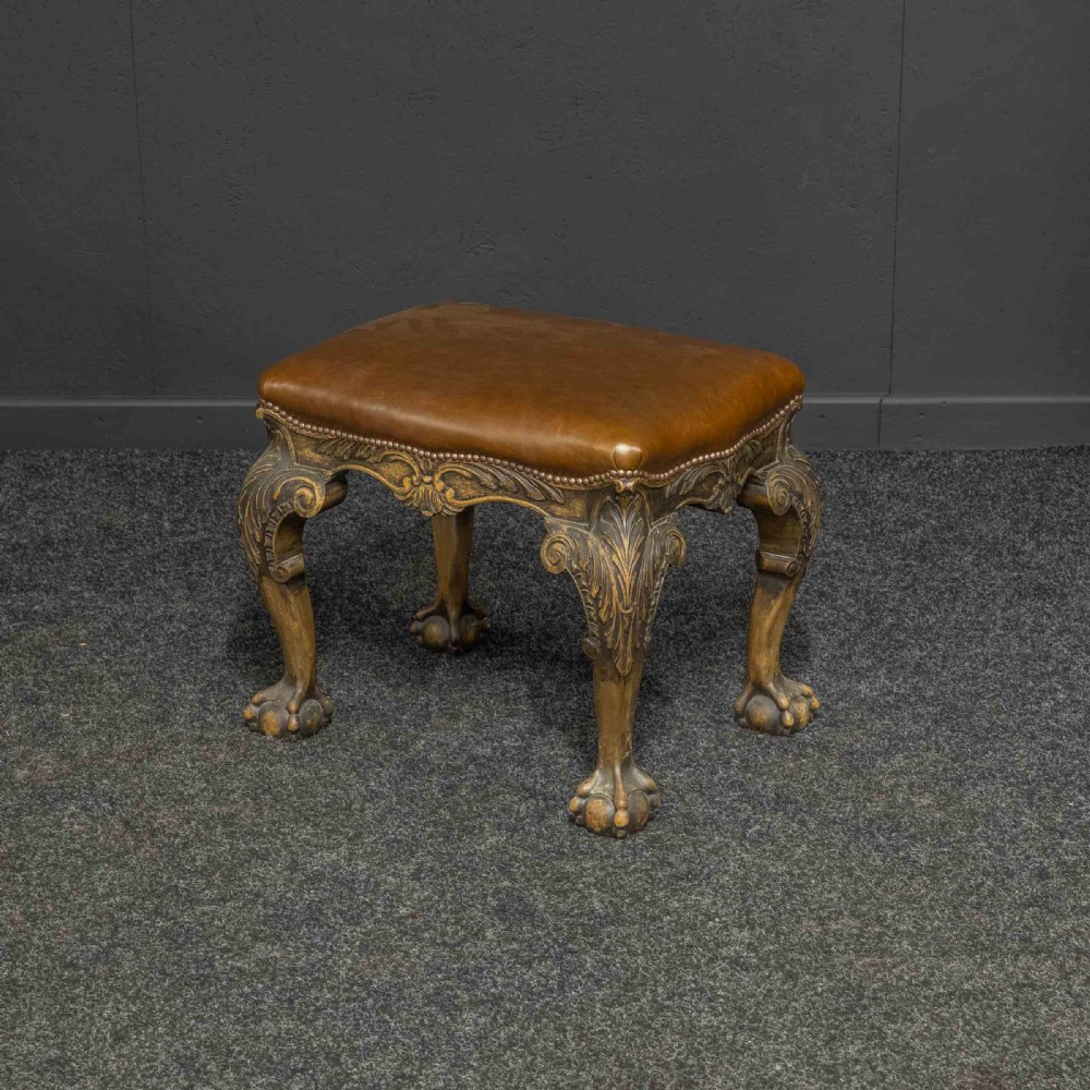 A low Chippendale style stool featuring a brown leather upholstered seat with brass stud detailing and dark carved cabriole legs ending in claw and ball feet. View IV