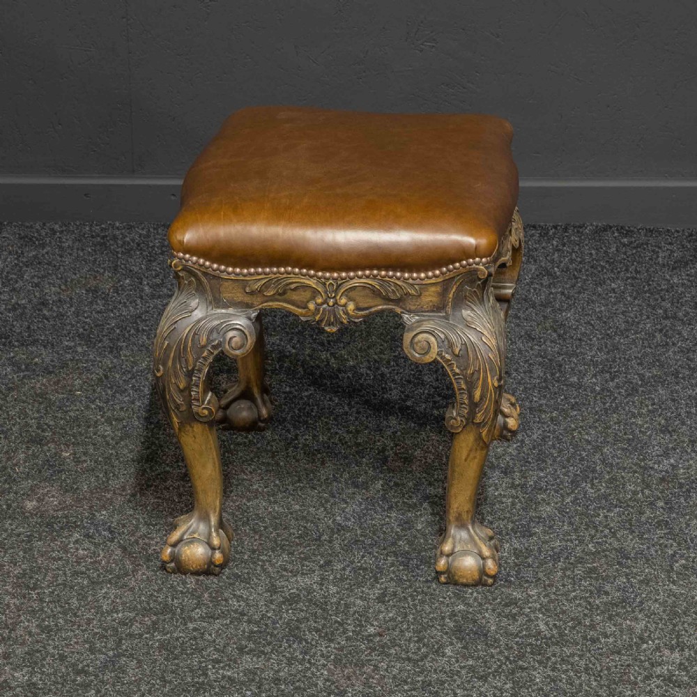 A low Chippendale style stool featuring a brown leather upholstered seat with brass stud detailing and dark carved cabriole legs ending in claw and ball feet. View V