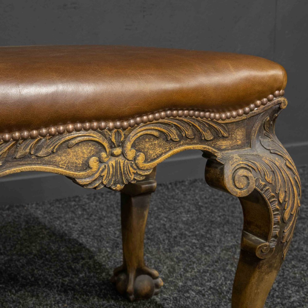 A low Chippendale style stool featuring a brown leather upholstered seat with brass stud detailing and dark carved cabriole legs ending in claw and ball feet. View XII