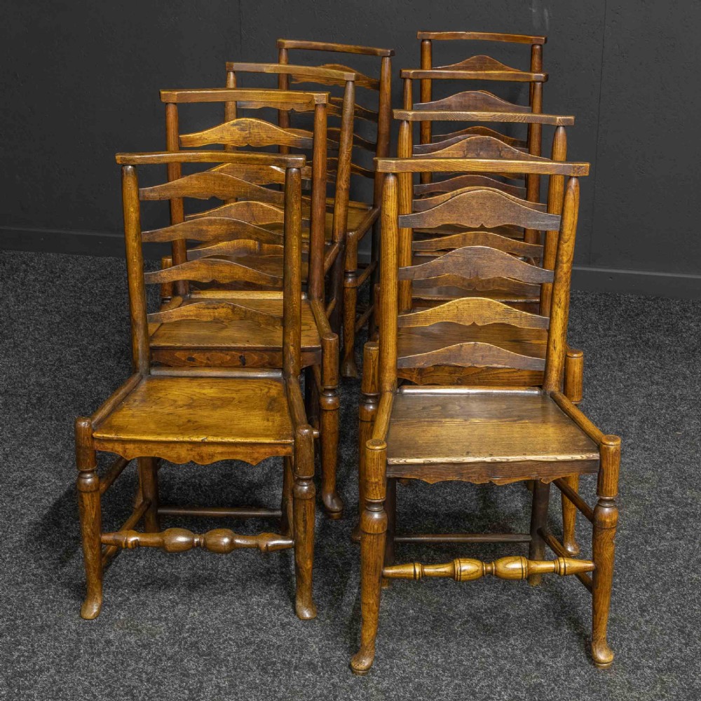 A set of eight Georgian oak dining chairs featuring wavy ladderbacks, solid panel seats, and turned front stretchers.
