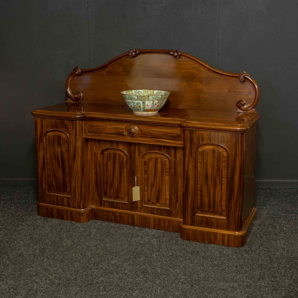 A Victorian mahogany sideboard featuring a carved backboard gallery, flame mahogany panelled doors, a central drawer, and a plinth base. View II
