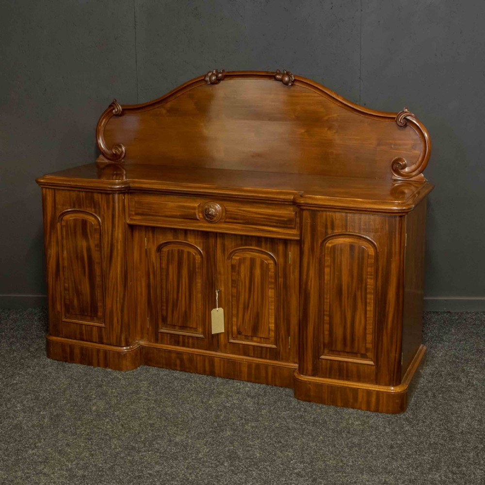 A Victorian mahogany sideboard featuring a carved backboard gallery, flame mahogany panelled doors, a central drawer, and a plinth base. View III