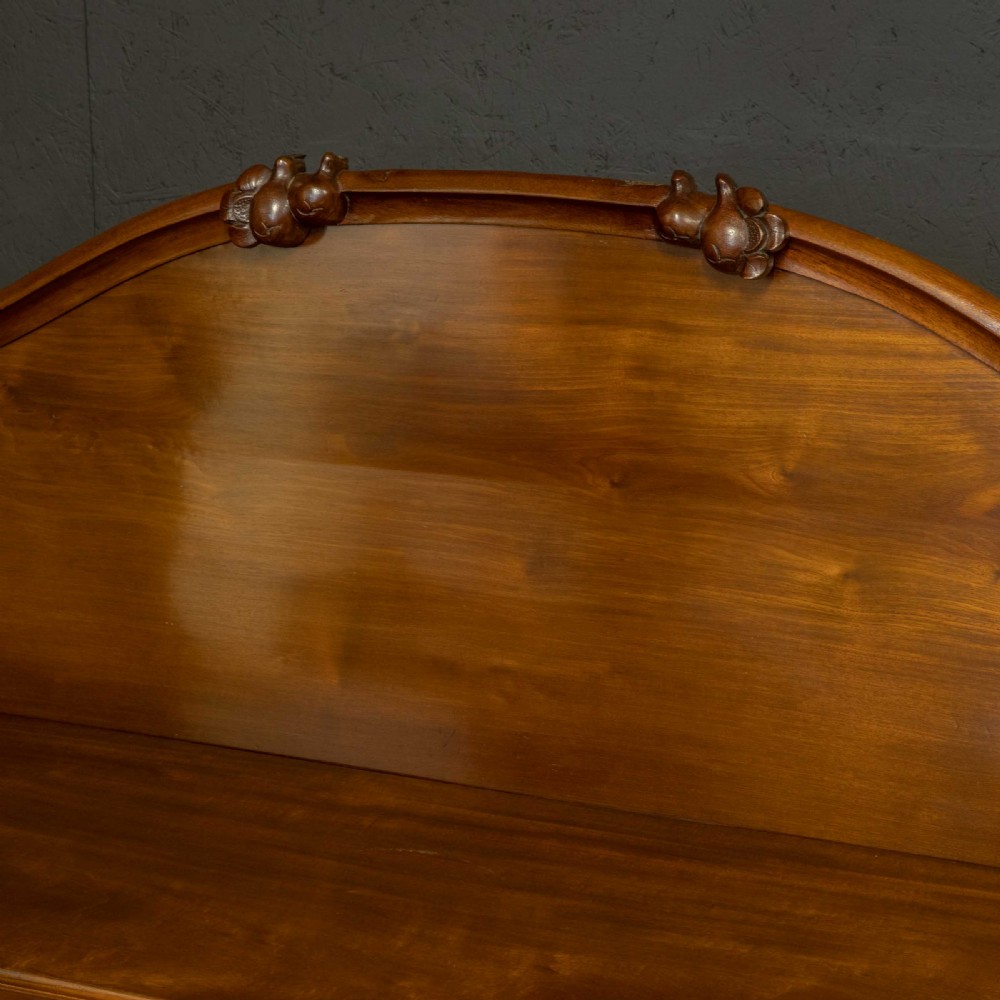 A Victorian mahogany sideboard featuring a carved backboard gallery, flame mahogany panelled doors, a central drawer, and a plinth base. View X