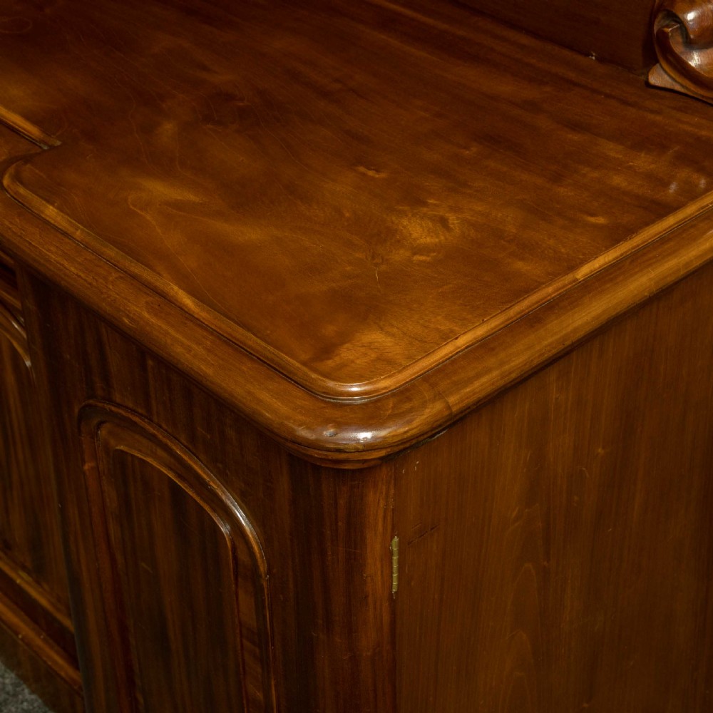 A Victorian mahogany sideboard featuring a carved backboard gallery, flame mahogany panelled doors, a central drawer, and a plinth base. View XVI