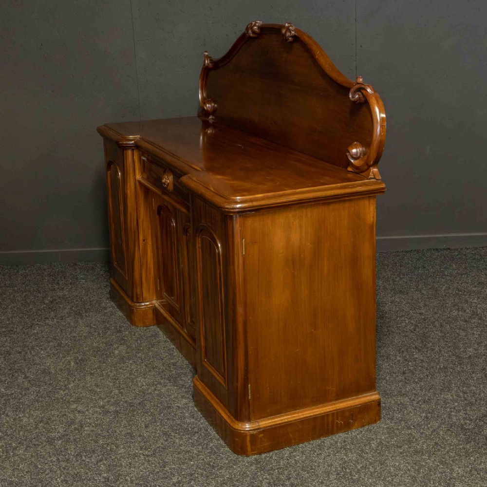 A Victorian mahogany sideboard featuring a carved backboard gallery, flame mahogany panelled doors, a central drawer, and a plinth base. View XVIII