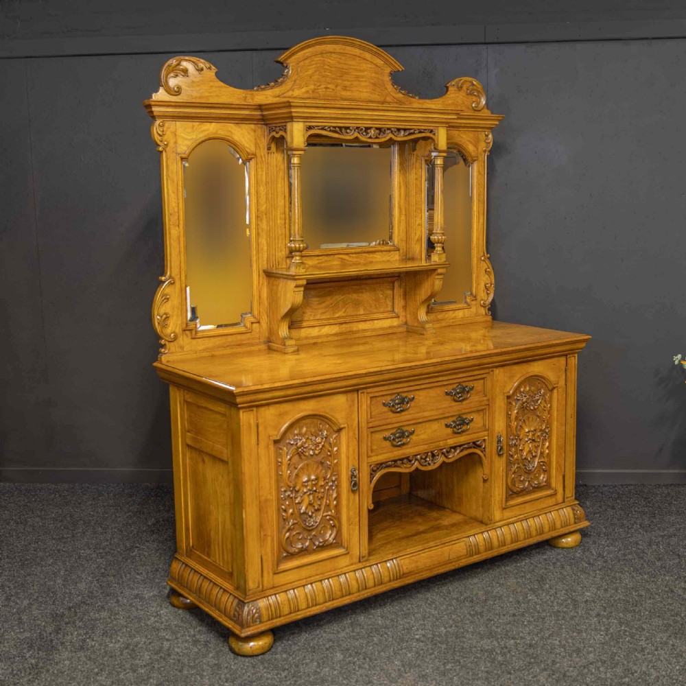Victorian pollard oak sideboard featuring a carved mirror-back superstructure, two central drawers, an open lower shelf, and flanking relief-carved cupboard doors.