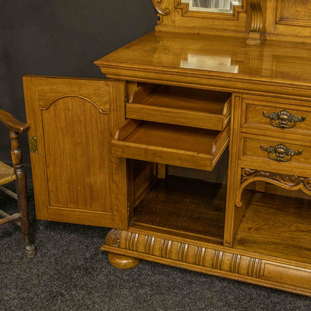 Victorian pollard oak sideboard featuring a carved mirror-back superstructure, two central drawers, an open lower shelf, and flanking relief-carved cupboard doors. View III