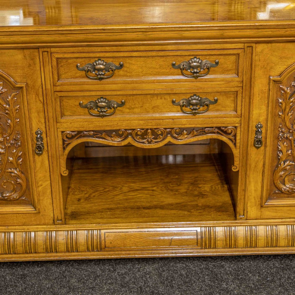 Victorian pollard oak sideboard featuring a carved mirror-back superstructure, two central drawers, an open lower shelf, and flanking relief-carved cupboard doors. View VII