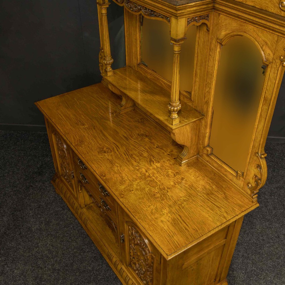 Victorian pollard oak sideboard featuring a carved mirror-back superstructure, two central drawers, an open lower shelf, and flanking relief-carved cupboard doors. View XIV